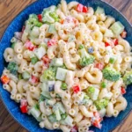 Creamy pasta salad with broccoli, cucumbers, peas, and red peppers in a blue bowl