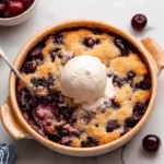 Easy cherry cobbler topped with vanilla ice cream in a rustic baking dish