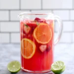 Glass pitcher of easy fruit punch with strawberries, orange slices, and lime