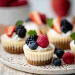 Mini cheesecakes topped with fresh berries and whipped cream on a serving tray
