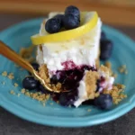 Slice of no-bake lemon blueberry dessert topped with fresh blueberries and lemon