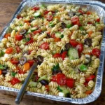 Large tray of pasta salad with vegetables, olives, and rotini pasta for parties