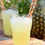 Refreshing pineapple lemonade served over ice with fresh pineapple in the background