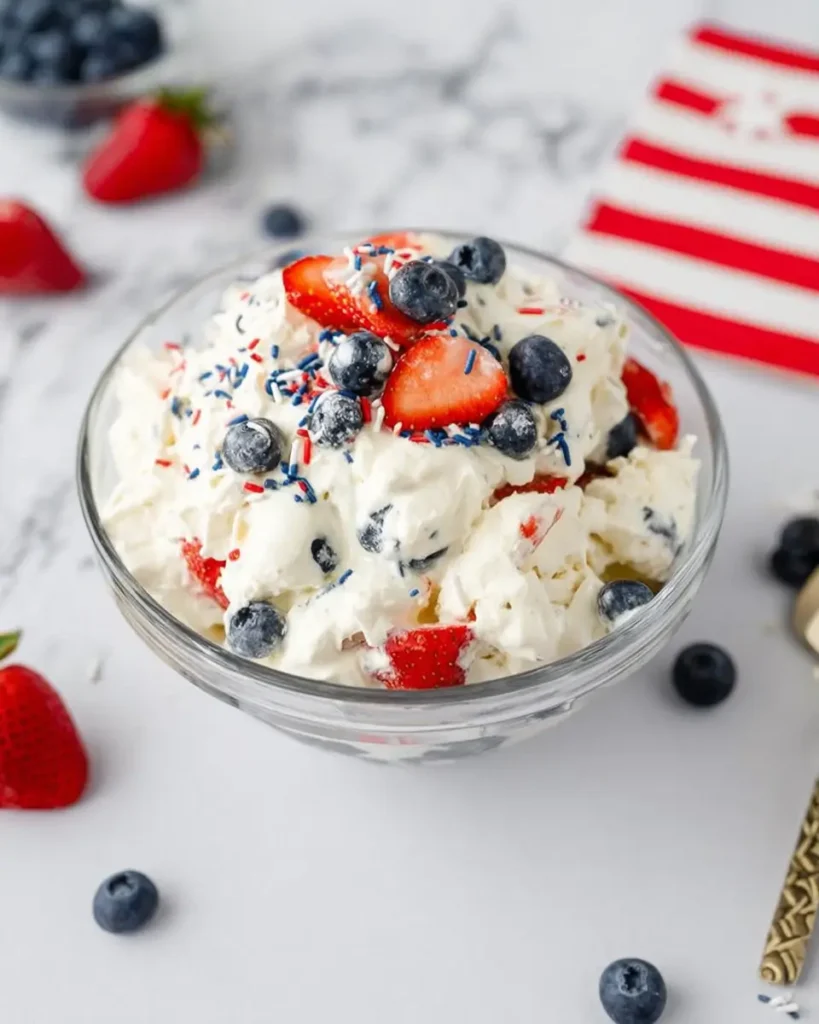 Red White and Blue Cheesecake Salad topped with strawberries, blueberries, and patriotic sprinkles in a glass bowl